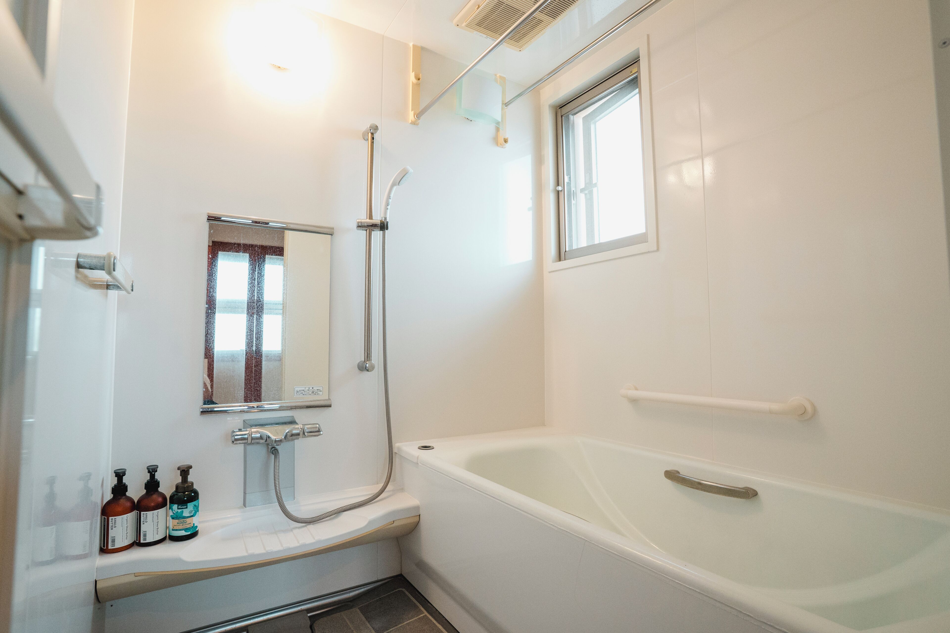 A bathroom with a bathtub, a shower, a window, and a mirror.