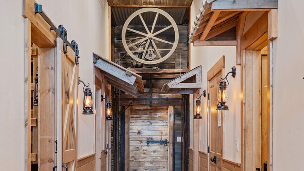 A wooden hallway with a large wooden wheel on the ceiling, wooden doors on either side, and a manhole cover in the center. - Historic Yellowstone Saloon |Sleeps 25, Hot Tub, Pool Table & More! (Ashton)