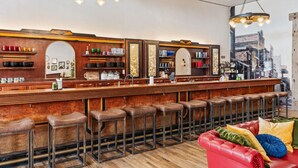 A bar area with wooden bar stools, a red leather couch, and a cityscape view through a large window. - Historic Yellowstone Saloon |Sleeps 25, Hot Tub, Pool Table & More! (Ashton)