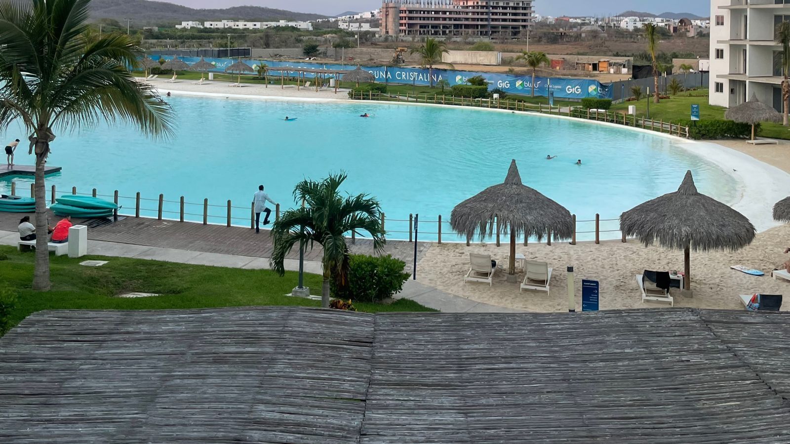 A swimming pool with a beach area, including lounge chairs and thatched umbrellas.