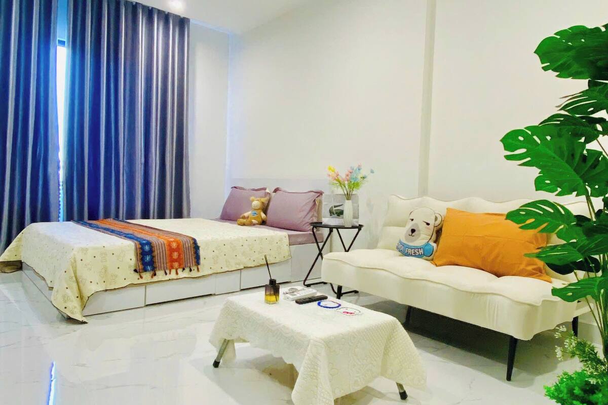 Una habitación moderna y luminosa con una cama, un sofá, una mesita y una planta grande.