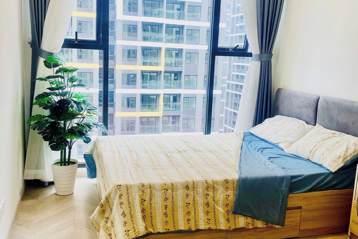 Un dormitorio con cama, una planta en maceta y vista a un edificio a través de un ventanal grande.