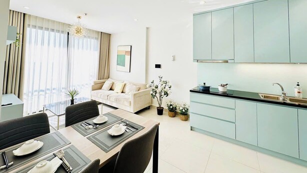 A modern living room with a sofa, dining table, and kitchen area with light blue cabinets. - Vinhomes Grand Park Luxury Apartments (Ho Chi Minh City)