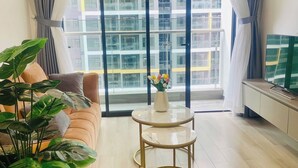 A modern living room with a sofa, a coffee table, and a large window with curtains. - Vinhomes Grand Park Luxury Apartments (Ho Chi Minh City)