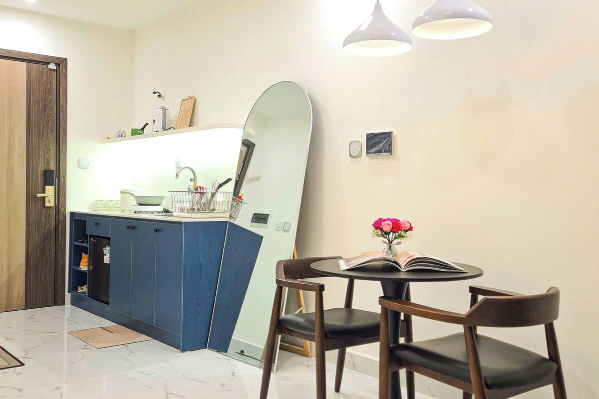 Una cocina moderna con un armario azul, una mesa redonda para comer con dos sillas y una lámpara colgante.