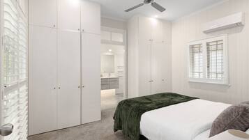 A bedroom with a bed, a ceiling fan, a window with blinds, and a closet with sliding doors.