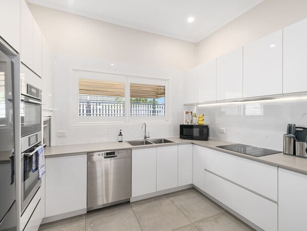 Una cocina moderna con armarios blancos, electrodomésticos de acero inoxidable, lavavajillas y una ventana con persianas.