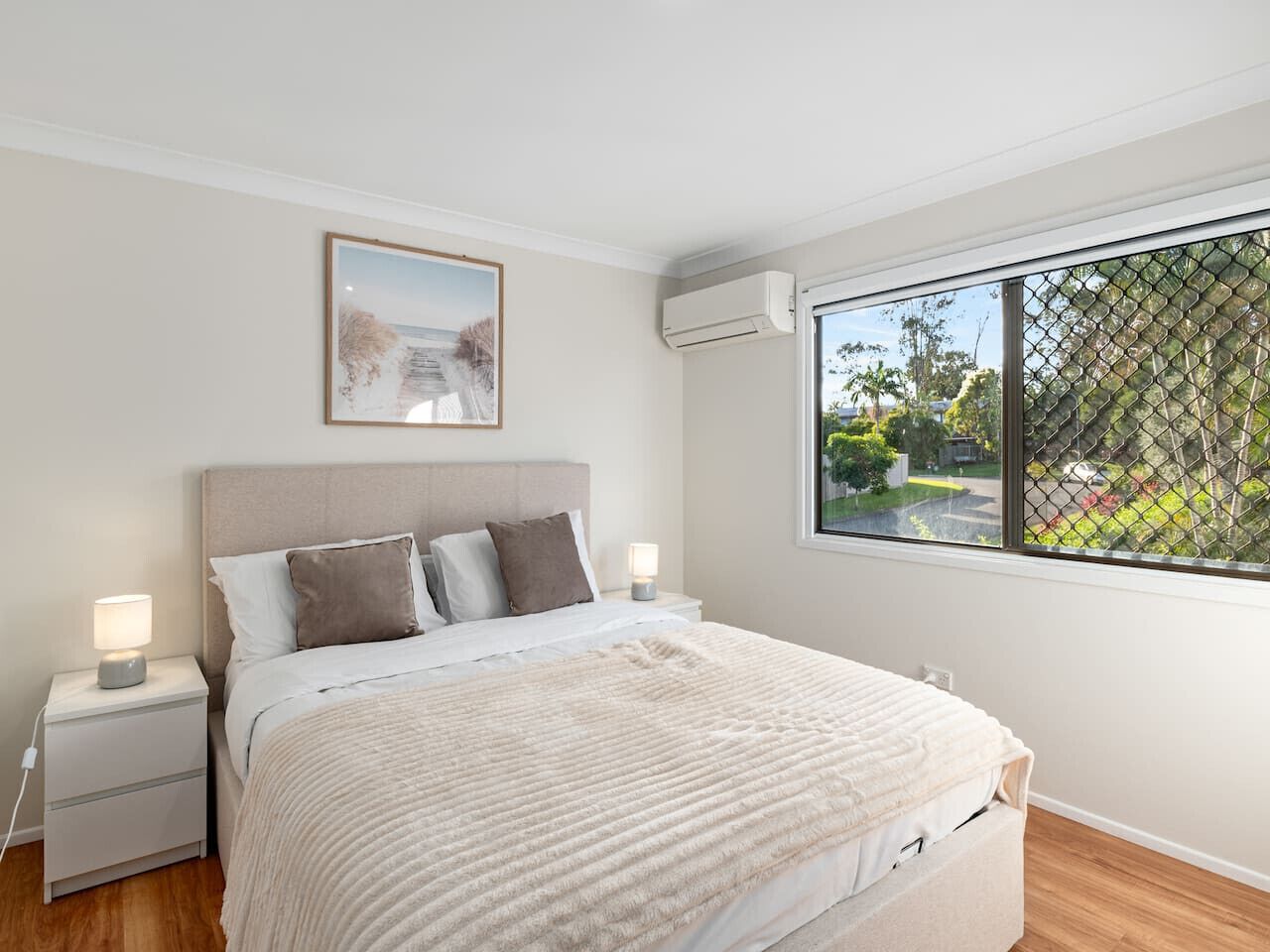 Un dormitorio con cama, mesitas de noche, una ventana con vistas y un aire acondicionado.