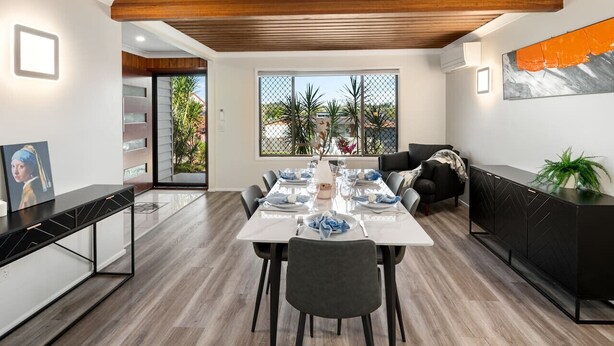 Un comedor moderno con techo de madera, una mesa larga dispuesta para seis personas y vistas al exterior a través de amplios ventanales.