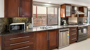 Una cocina moderna con armarios de madera oscura, lavavajillas de acero inoxidable, horno empotrado y microondas.
