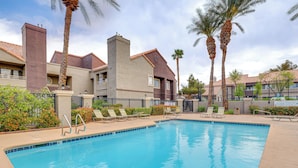 A swimming pool with lounge chairs and palm trees, surrounded by buildings with brick and stucco exteriors.