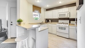 A modern kitchen with white cabinets, a central island with stools, a microwave, stove, and a window with a view.