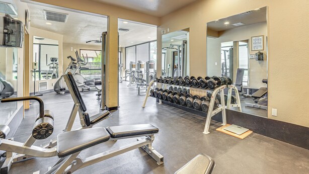 A gym with exercise equipment, a mirror, and a rack of dumbbells.