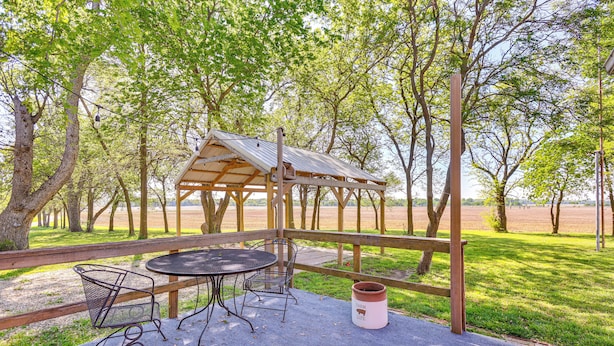 A covered outdoor seating area with metal chairs and a table, surrounded by trees and a grassy field. - Countryside Escape 14 Mi to Milford & Geary Lakes! (Chapman)
