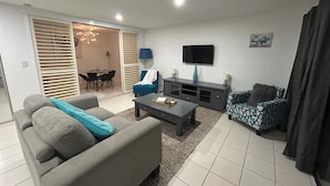 A living room with a sofa, a coffee table, a TV, and a dining area with a table and chairs.