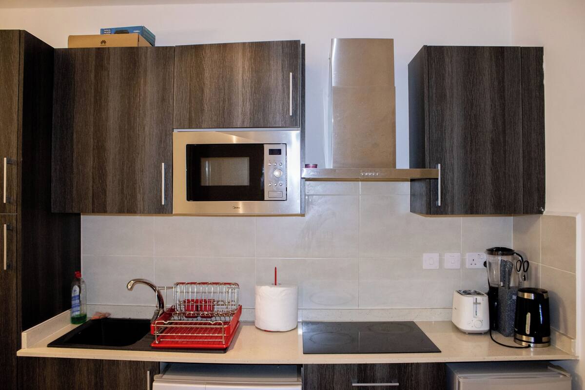 Eine moderne Küche mit dunklen Holzschränken, einer Edelstahl-Mikrowelle, einem Toaster und einer Kaffeemaschine auf der Arbeitsfläche.