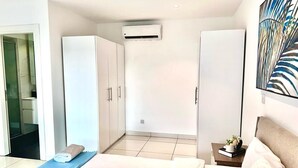 Et moderne hotelværelse med en seng, en blå yogamåtte, et lille bord med en bog og en plante, samt et stort vindue.