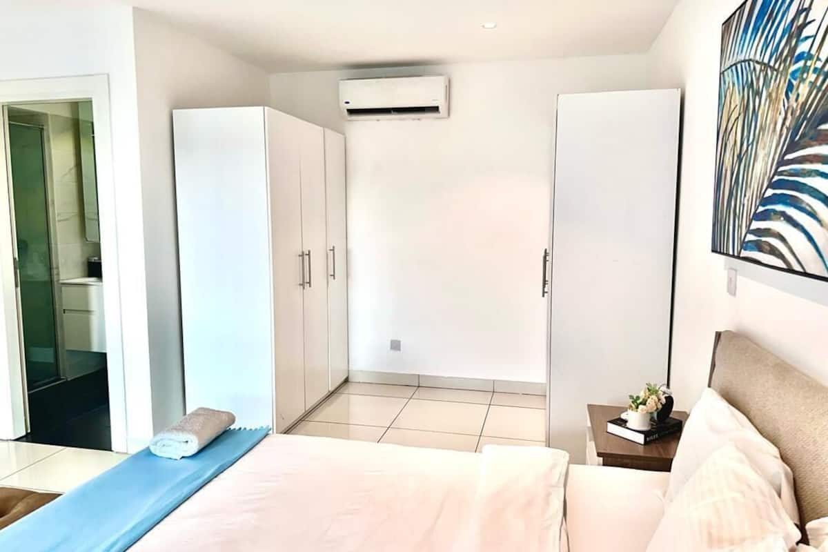 Ein modernes Hotelzimmer mit einem Bett, einer blauen Yogamatte, einem kleinen Tisch mit einem Buch und einer Pflanze sowie einem großen Fenster.