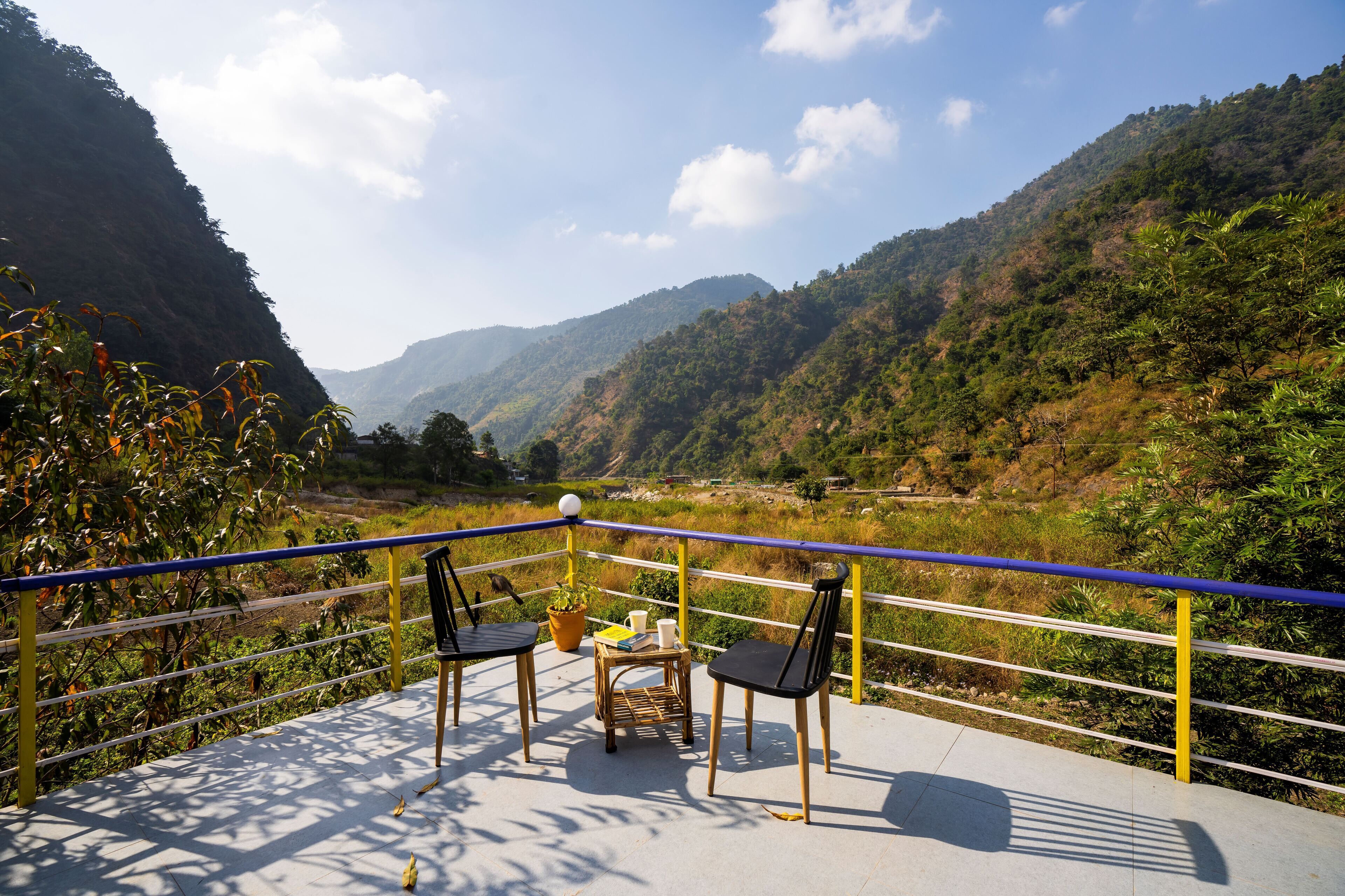 A balcony with two chairs and a table, overlooking a mountainous landscape.
