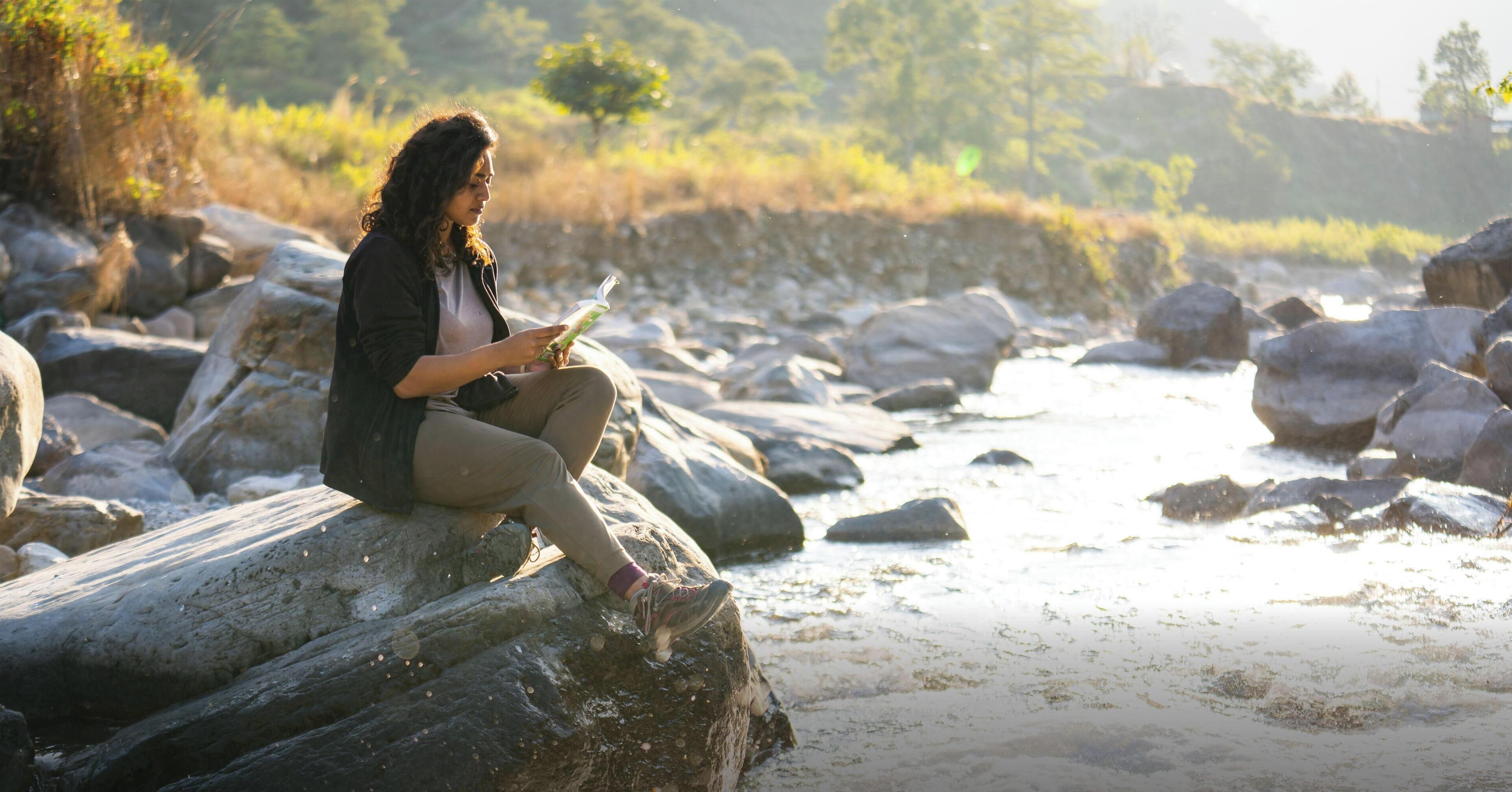 A person sitting on a rock by a river.