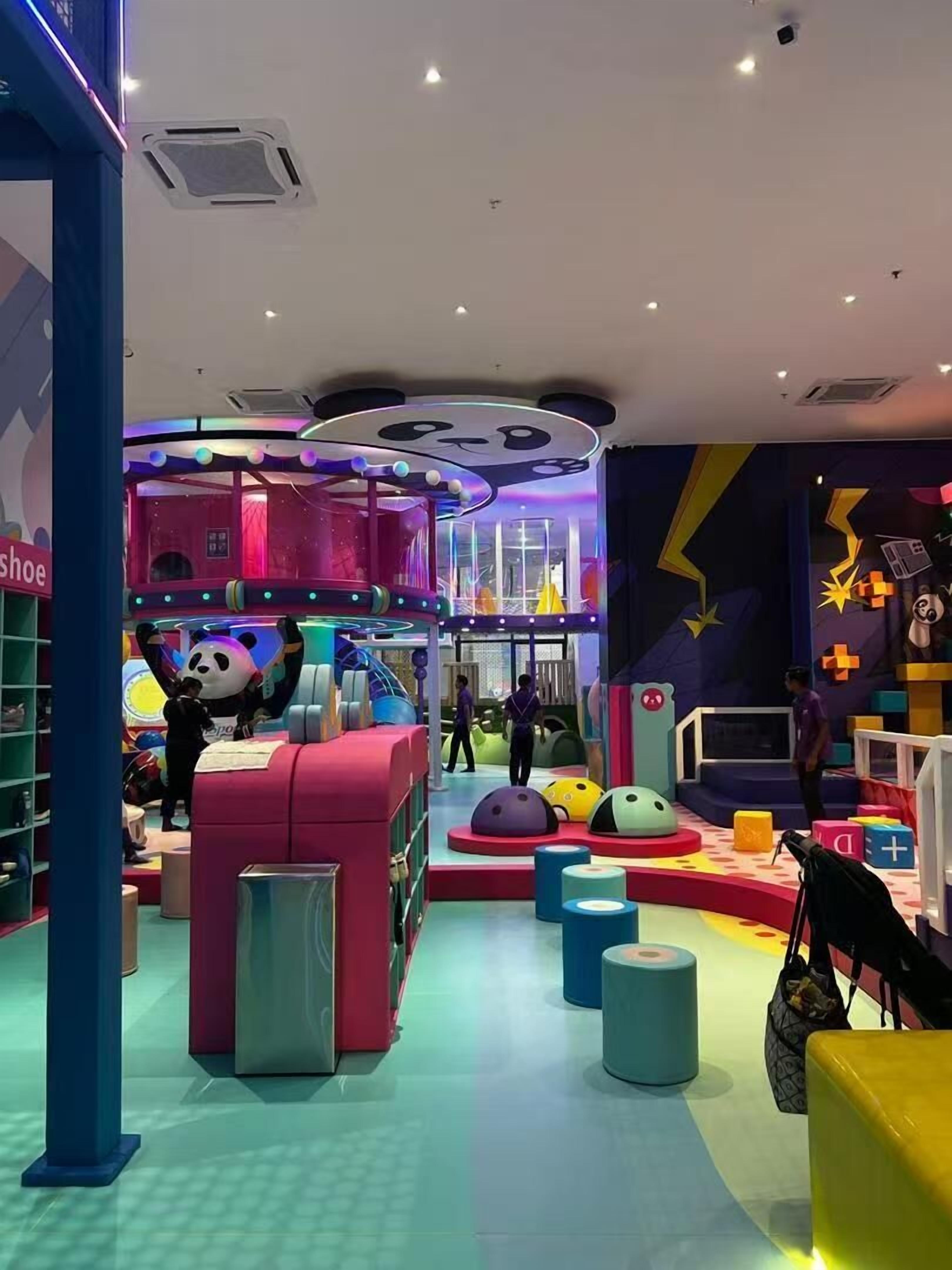 A brightly lit indoor play area with colorful play structures and a panda mascot.