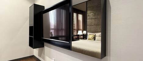 Una habitación de hotel moderna con un televisor de pantalla plana grande montado en la pared, una cama con cabecera y una mesita de noche con lámparas.