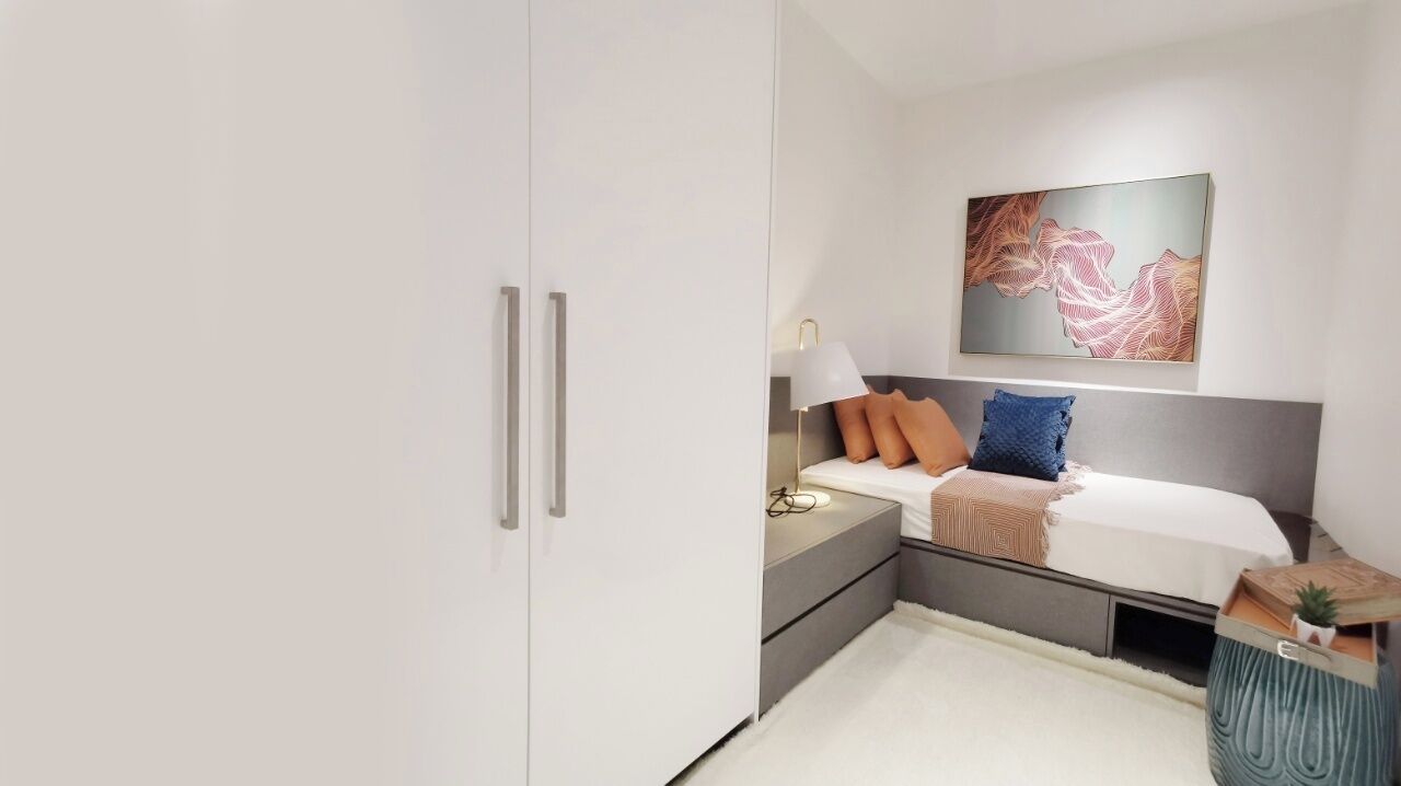 Un dormitorio con cama, mesita de noche, lámpara y una obra de arte en la pared.
