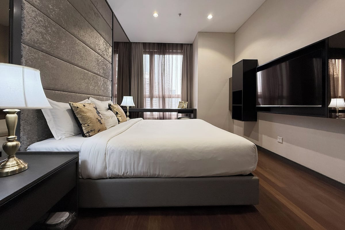 Ein modernes Hotelzimmer mit einem großen Bett, einem flachbildfernseher an der Wand und einem Schreibtisch mit Lampe.