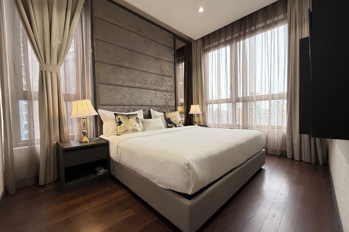 Ein modernes Schlafzimmer mit einem großen Bett, Holzboden und Blick auf die Stadt durch große Fenster.