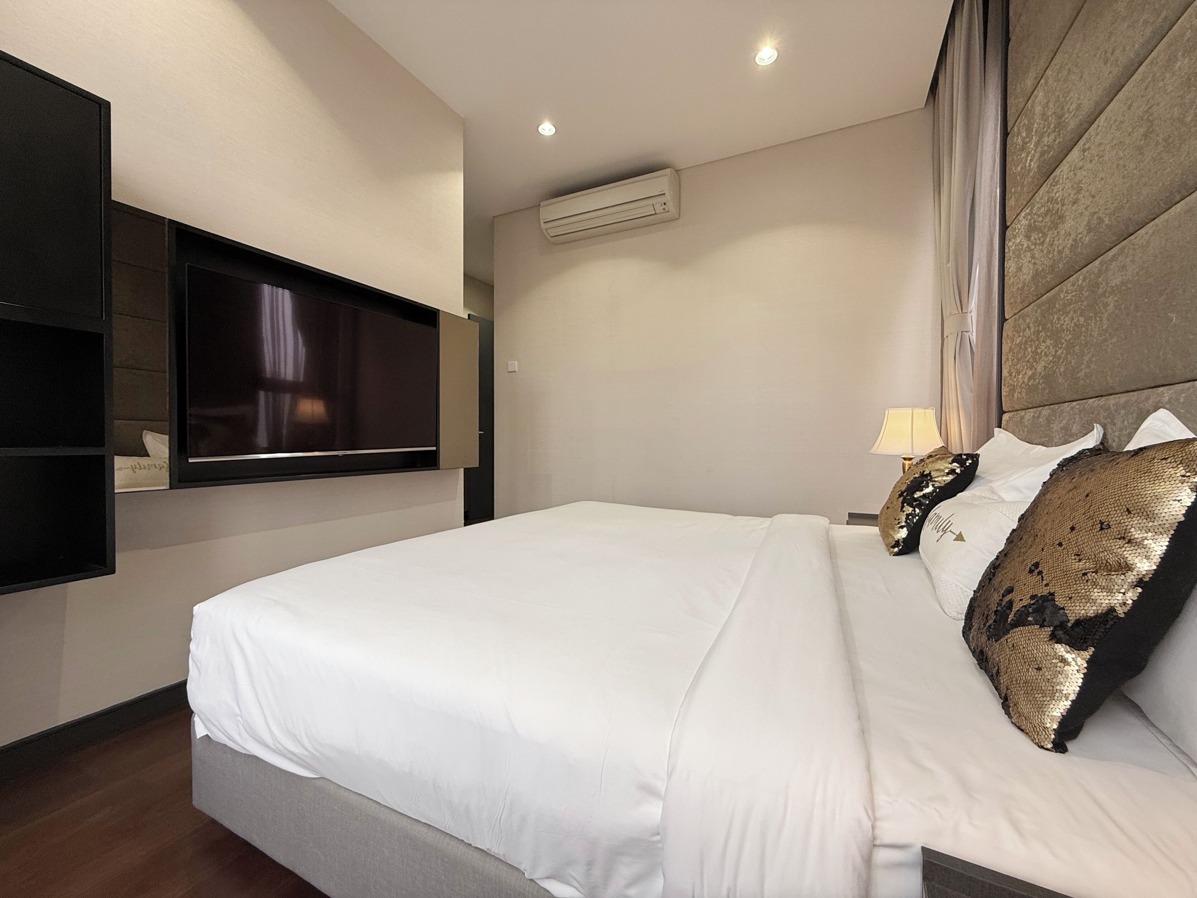 A modern hotel room with a large bed, a mounted TV, and an air conditioning unit on the wall.