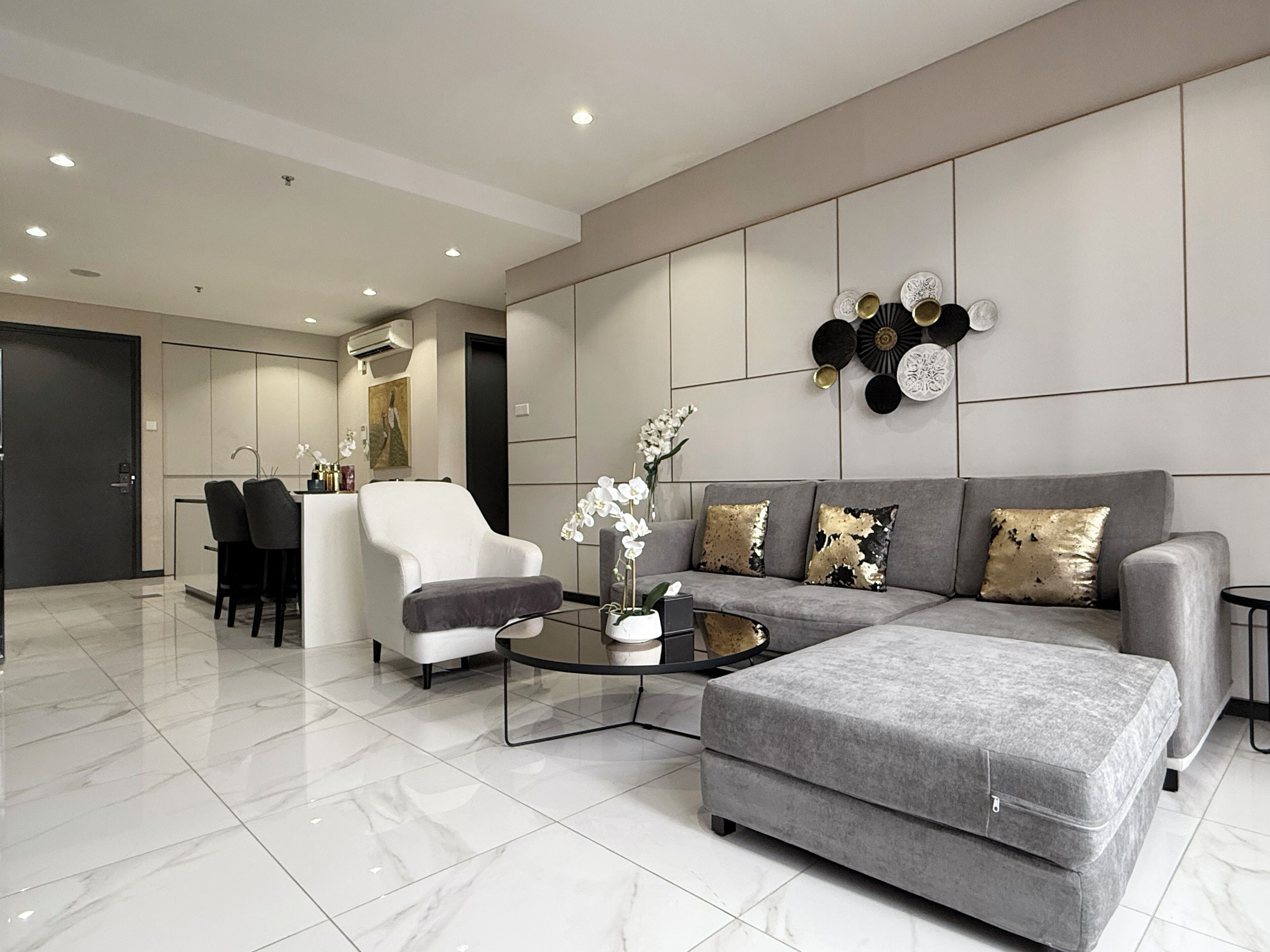 A modern living room with a grey sofa, a coffee table, and a grey ottoman. There is a white armchair and a black chair in the background.