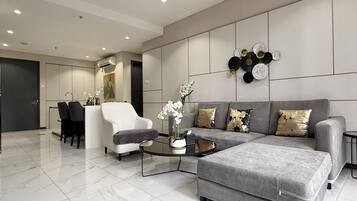 A modern living room with a grey sofa, a coffee table, and a grey ottoman. There is a white armchair and a black chair in the background.