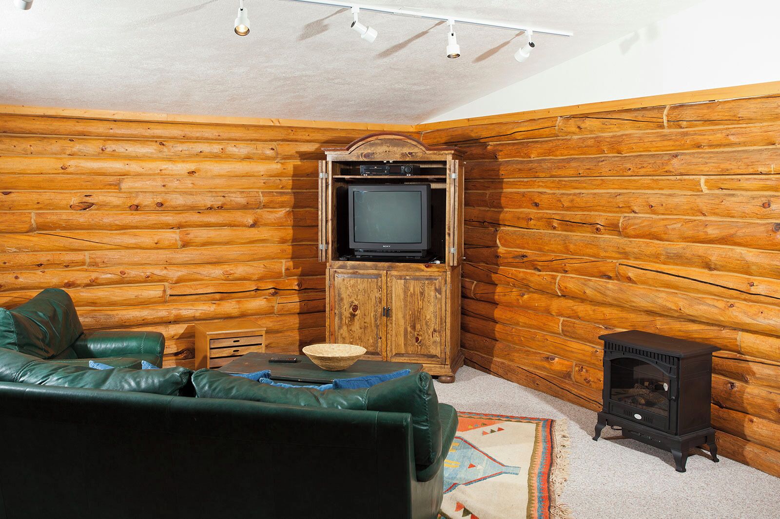Interior de una cabaña de troncos con un sofá de cuero verde, un televisor, una chimenea y una cesta tejida.