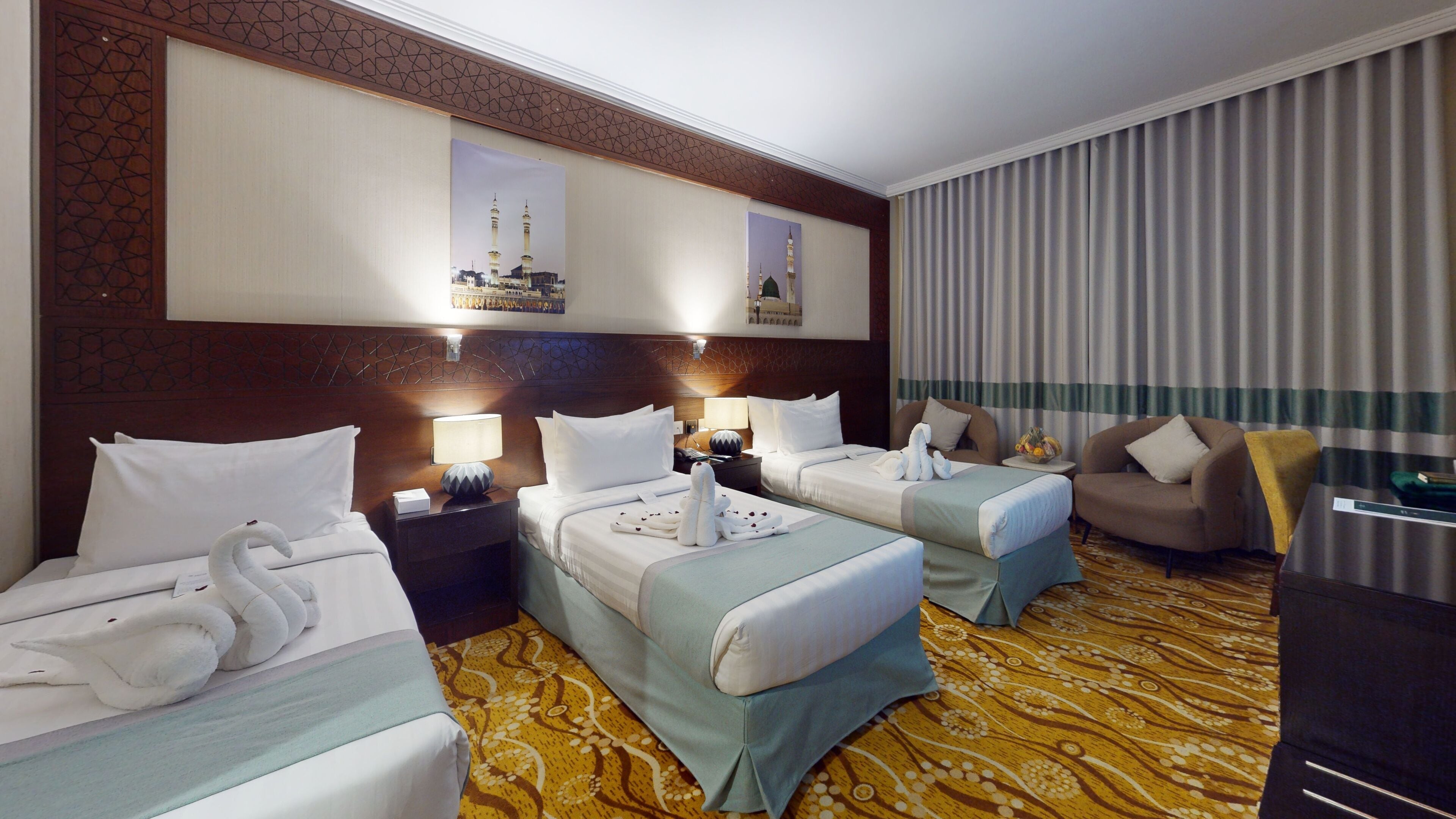 A hotel room with two beds, a sofa, a desk, and a large window with curtains.