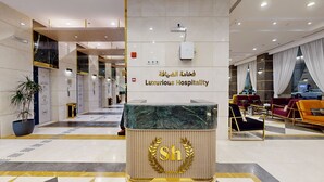 Un vestíbulo de hotel con mostrador de recepción, un letrero que dice “Luxurious Hospitality” y un área de estar con sofás.
