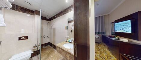 A modern bathroom with a glass-enclosed shower, a white toilet, a marble vanity, and a television mounted on the wall.