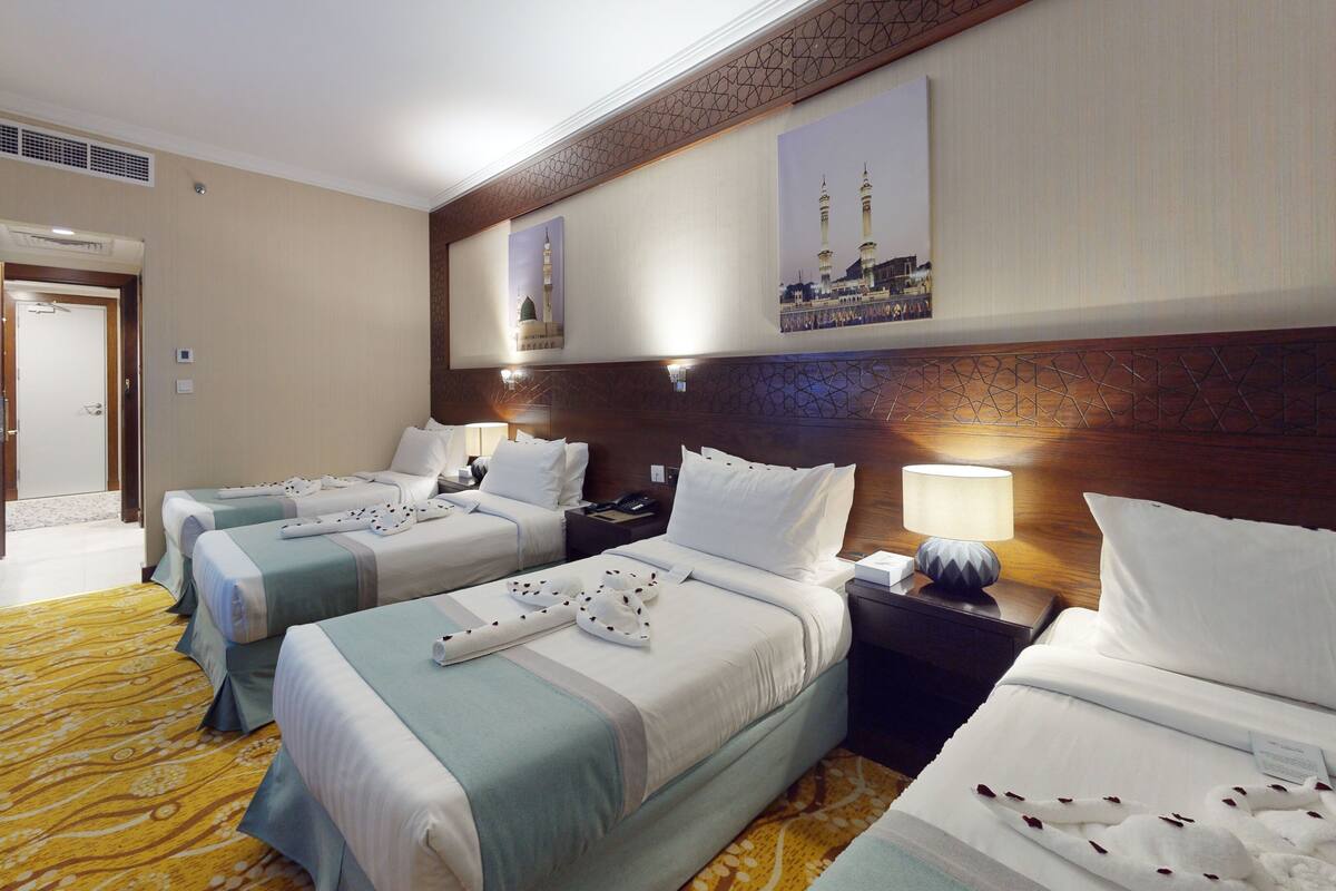 A hotel room with two beds, a desk, a chair, a lamp, and a picture of a mosque on the wall.