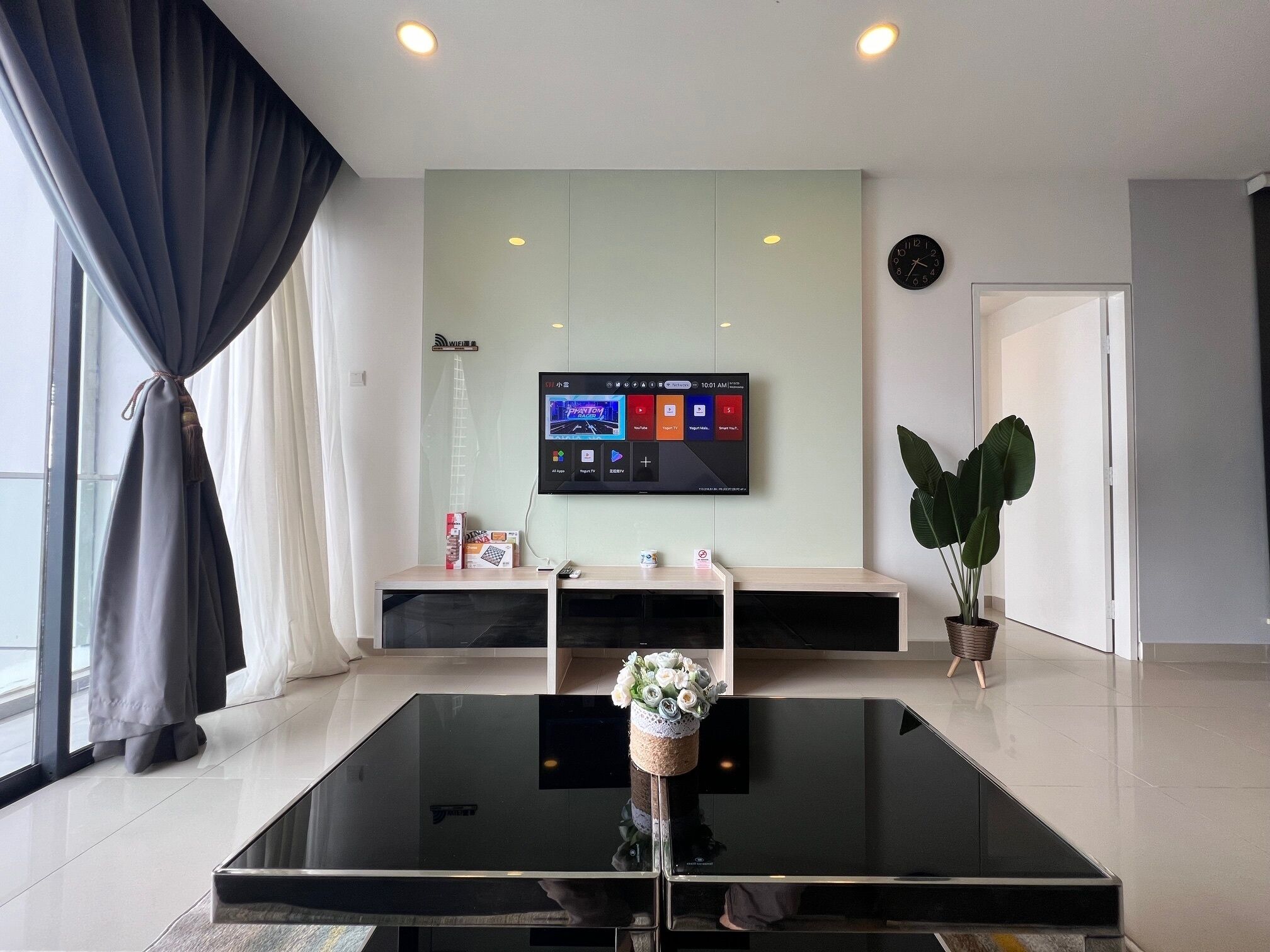 Una sala de estar moderna con un televisor de pantalla plana en la pared, una mesa de centro de vidrio y una planta en maceta.