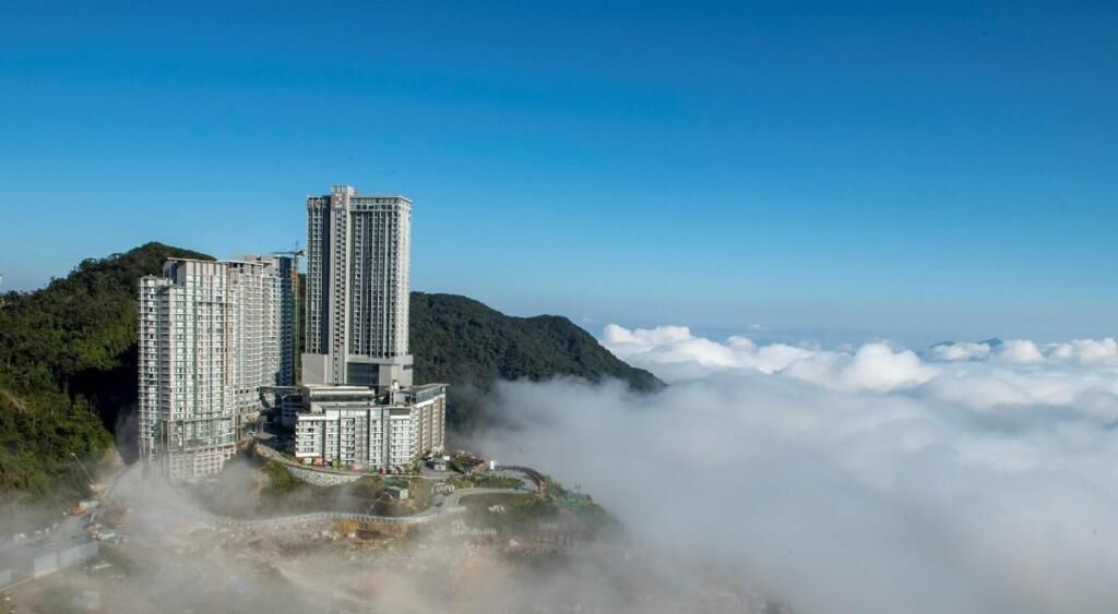 A high-rise hotel complex with multiple buildings, surrounded by lush greenery and clouds.