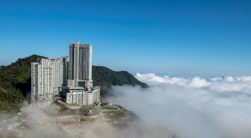 A high-rise hotel complex with multiple buildings, surrounded by lush greenery and clouds.