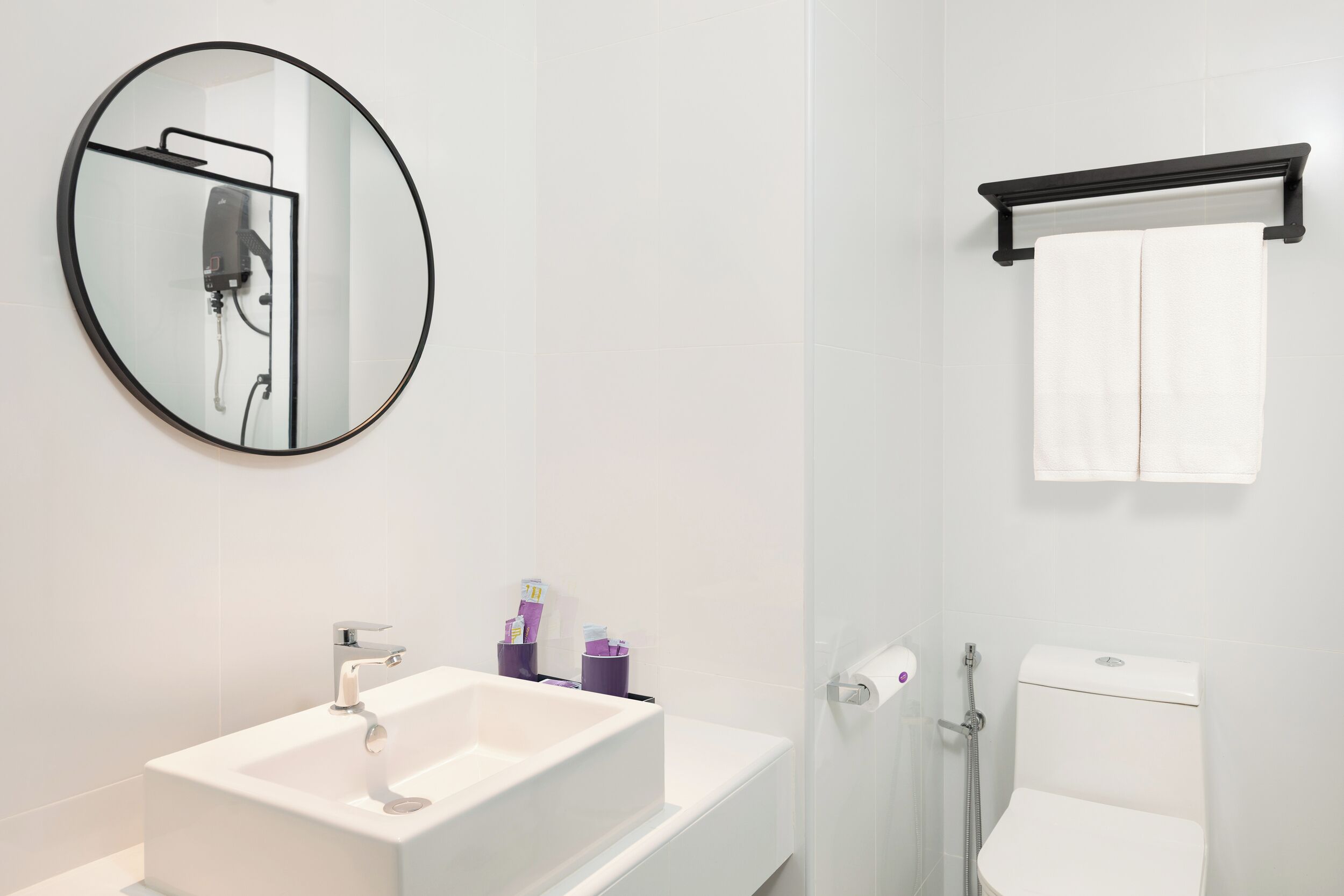 A modern bathroom with a white sink, a round mirror, a toilet, and a glass shower enclosure.