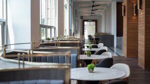 A modern restaurant interior with round tables and booths, potted plants, and a wooden accent wall. - Quest Hotel Midport Port Dickson (Port Dickson)