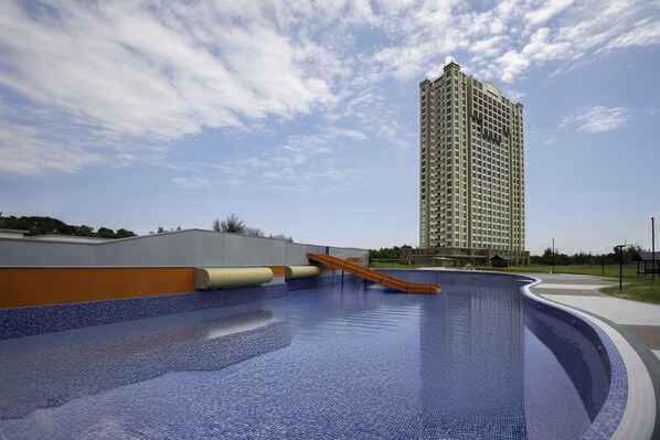 Una piscina con tobogán, rodeada por un edificio y una torre residencial alta.