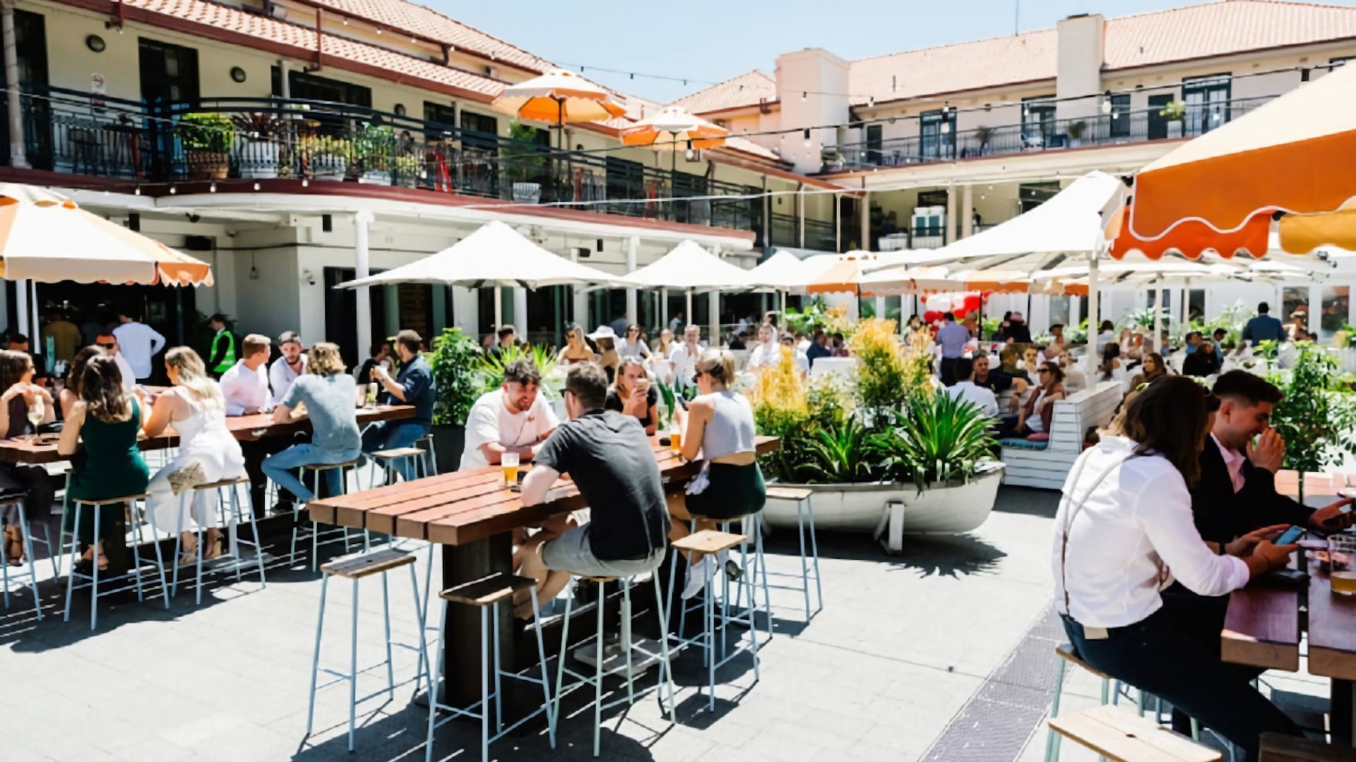 An outdoor dining area with multiple tables and chairs, surrounded by umbrellas and potted plants.