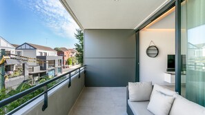 A balcony with a sofa, a TV, and a view of neighboring buildings.