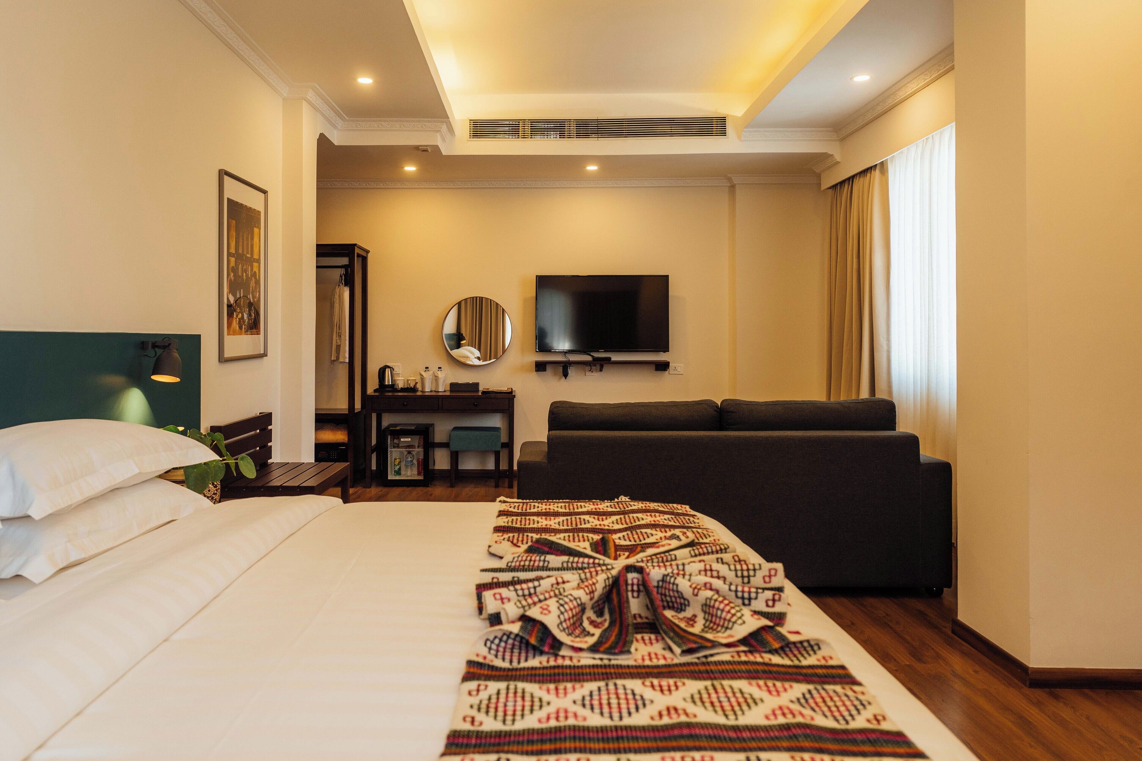 A hotel room with a large bed, a sofa, a TV, and a desk with a mirror.