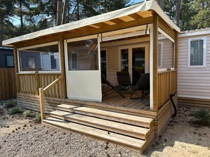 Uma casa móvel com deck de madeira, varanda coberta e porta deslizante.