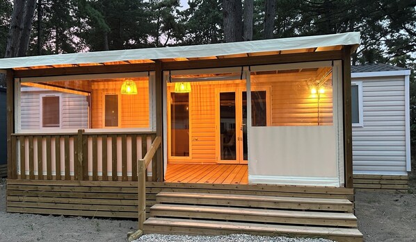 Uma cabana de madeira com varanda coberta, porta de correr e um pequeno galpão anexo.