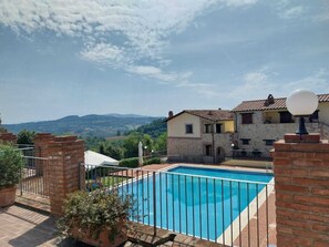 Relax by the serene pool surrounded by lush greenery and distant hills.