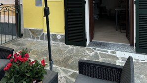 Un espace extérieur aménagé avec une table et des chaises, un pot de fleurs orné de fleurs rouges et un grand parasol.